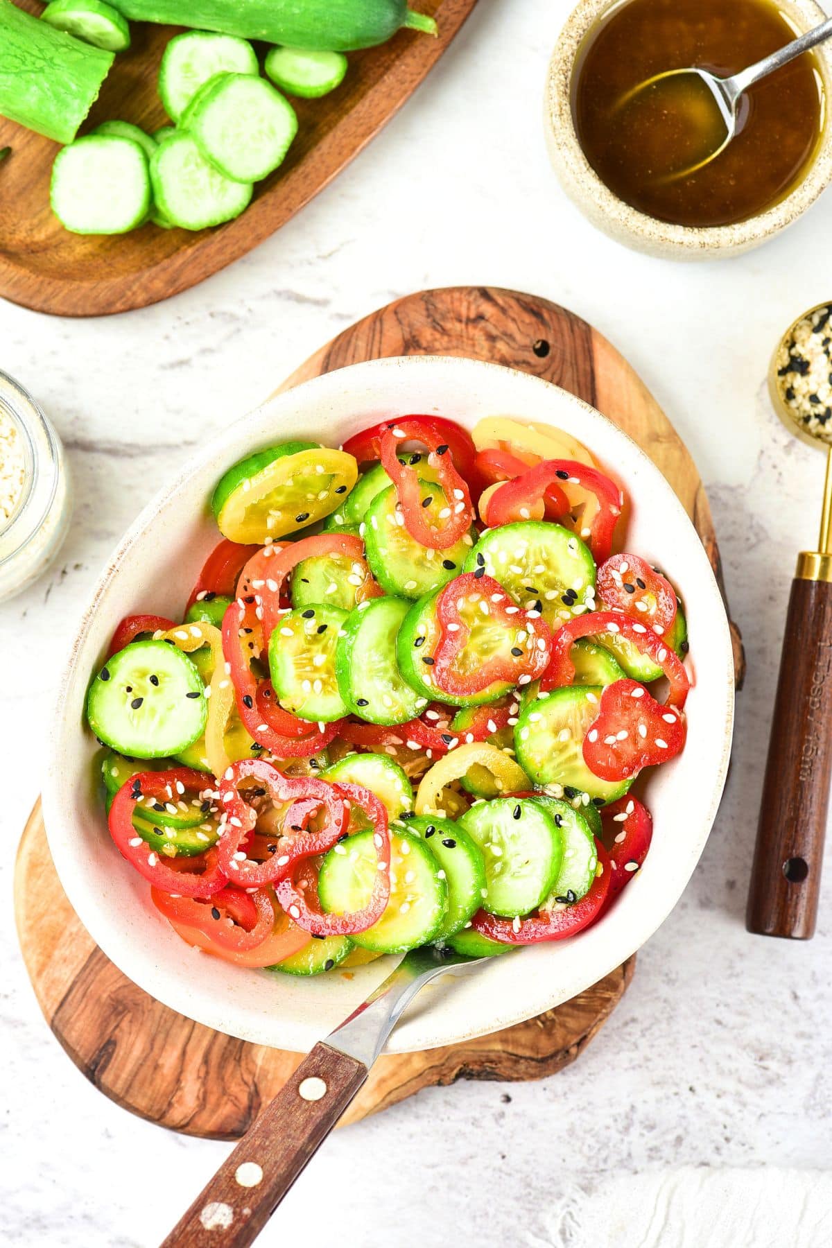 Top down view of a bowl of cucumber pepper salad on wooden board.