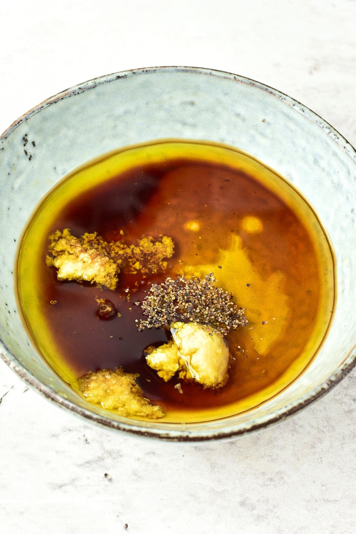 Soy sauce, olive oil, grated ginger, minced garlic and ground black pepper in bowl.