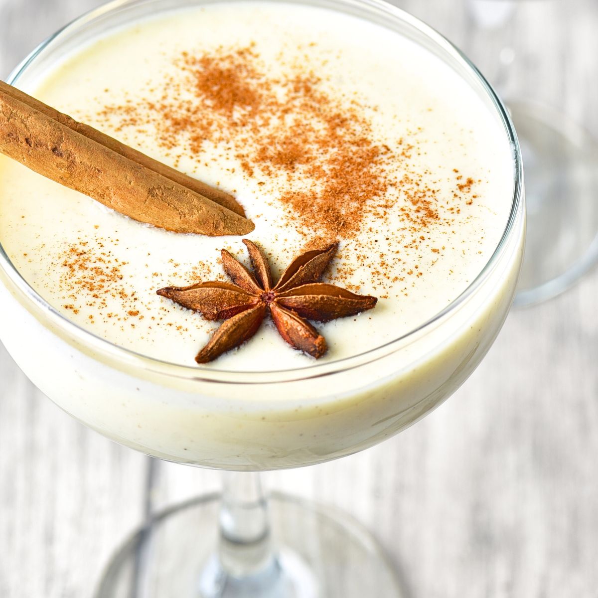 A glass of eggnog with cinnamon stick and star anise.