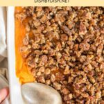 Top down view of hand reaching for a baking dish with sweet potato casserole