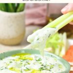 Dipping a celery stick into a bowl of dairy-free tzatziki sauce