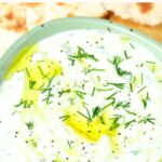 Top down view of a bowl of tzatziki sauce topped with fresh dill and olive oil