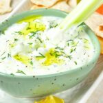 Dipping celery stick into a bowl of dairy-free tzatziki