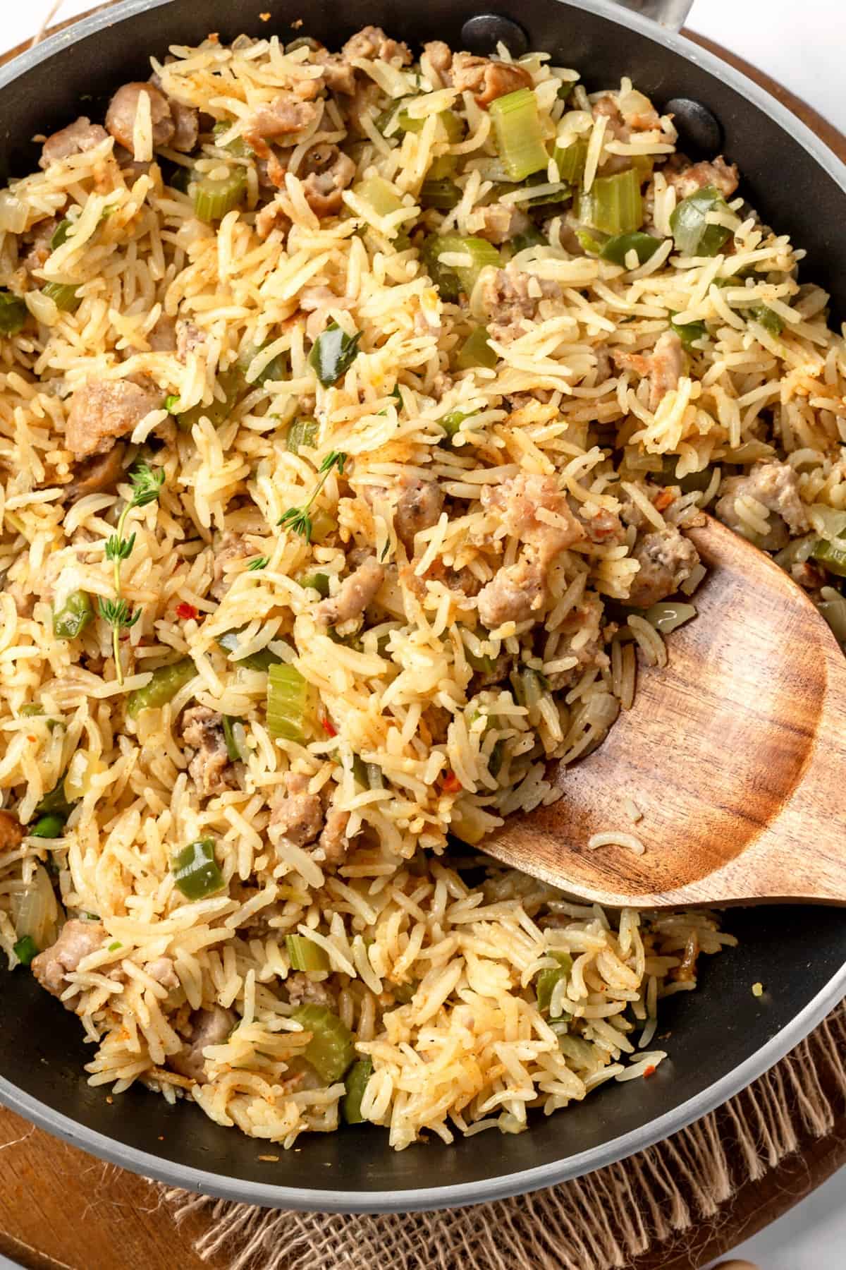 Scooping out dirty rice with a wooden spoon from a skillet.