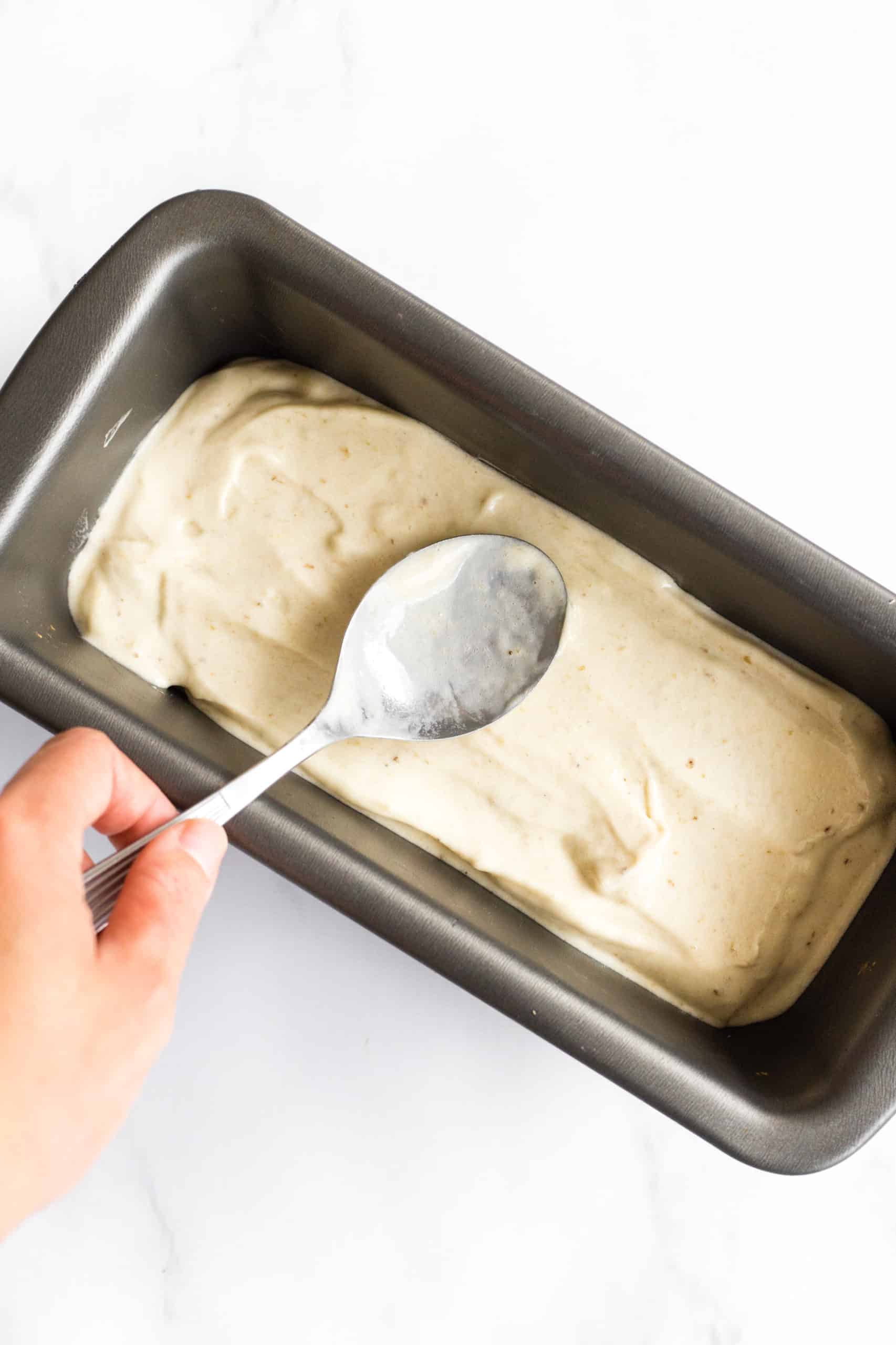Using a spoon to spread out banana ice cream in a loaf pan to be frozen