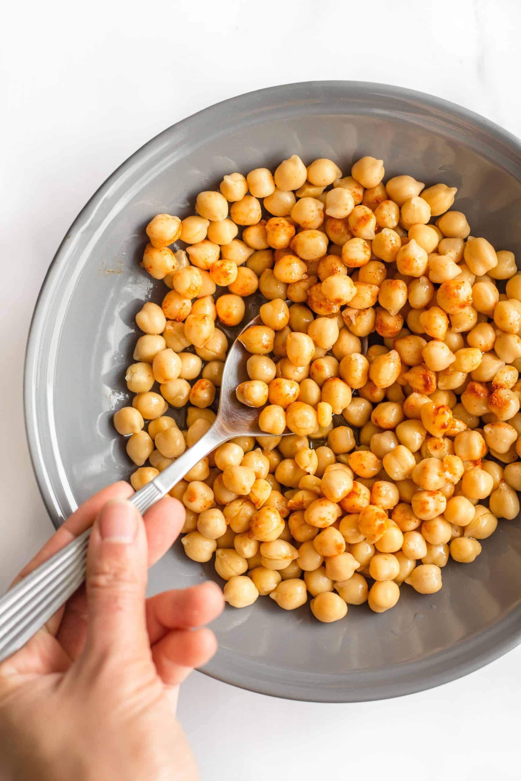 Mixing chickpeas with paprika with a spoon in a grey bowl.