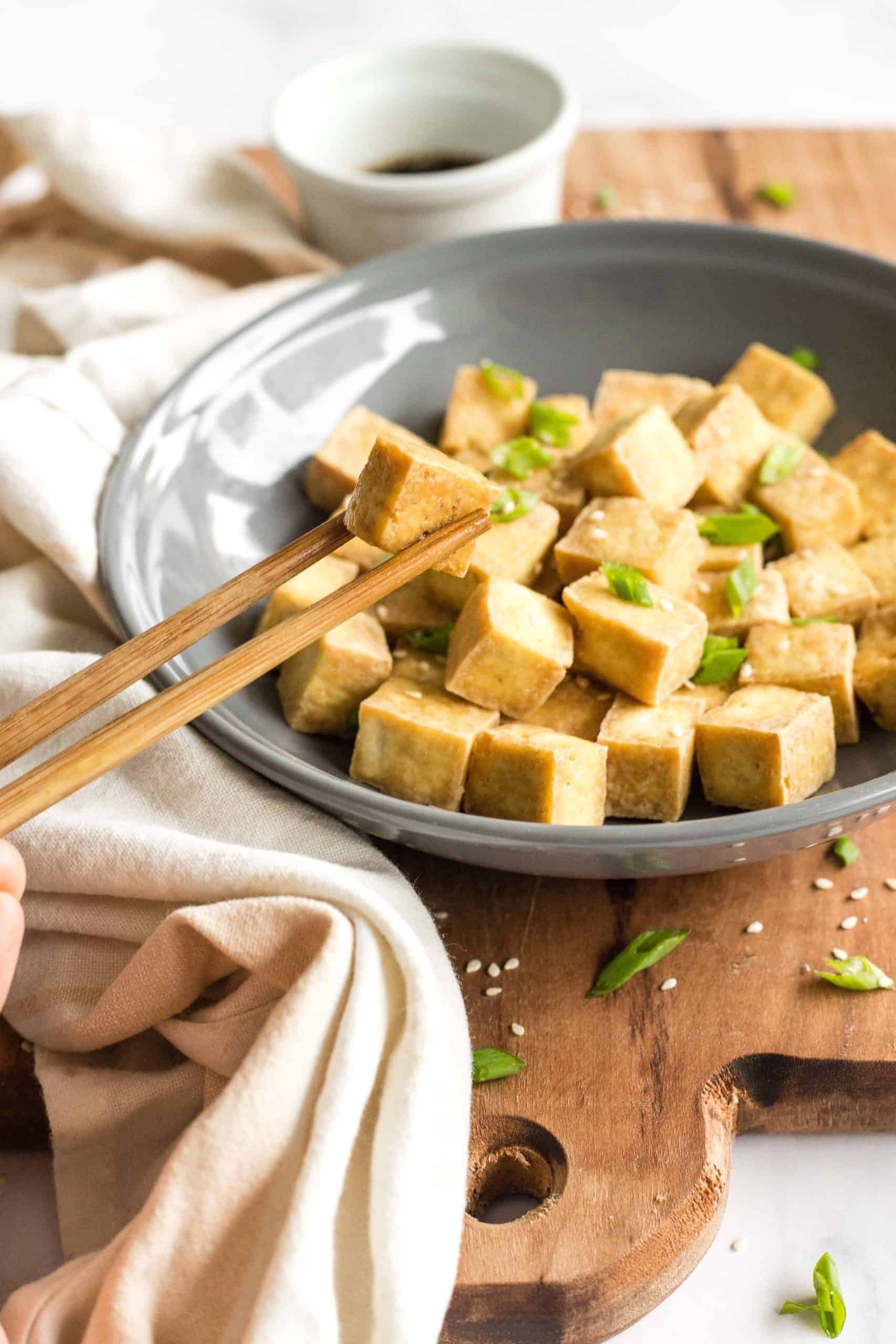 A pair of chopsticks picking up a tofu cube from a bowl.