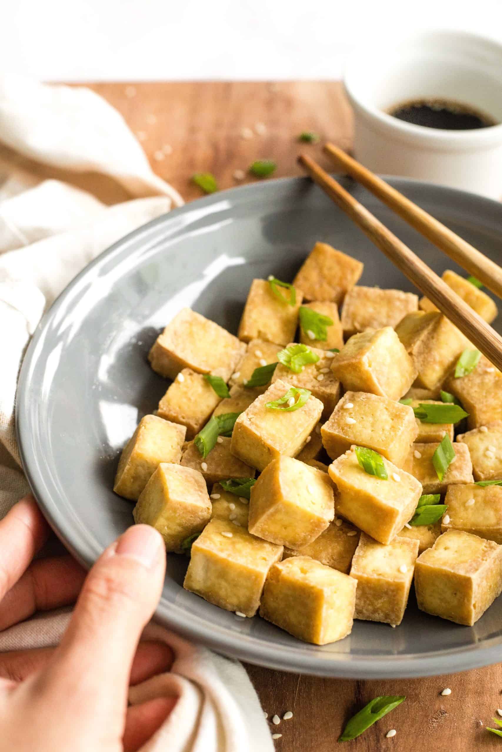 Hand holding a grey bowl of crispy air fryer tofu nuggets. 