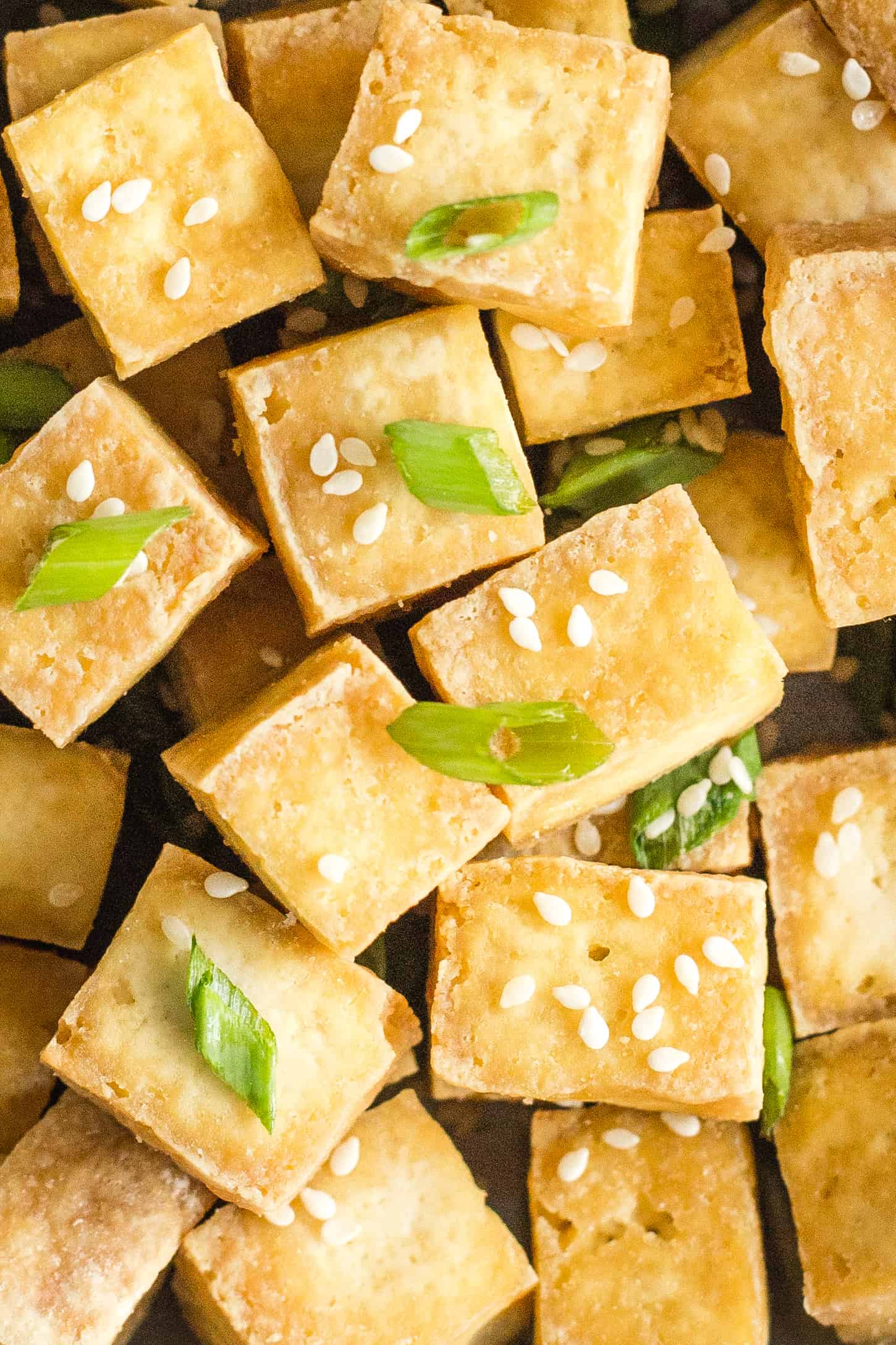 Up close shot of crispy air fryer tofu sprinkled with sesame seeds and chopped spring onions.