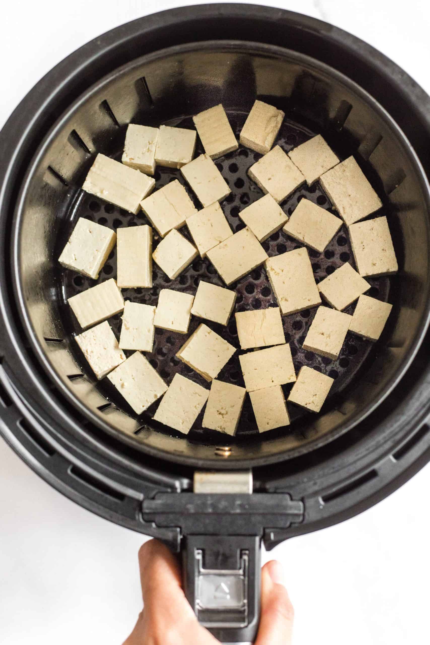 Tofu cubes in a single layer in the air fryer basket ready to be cooked.