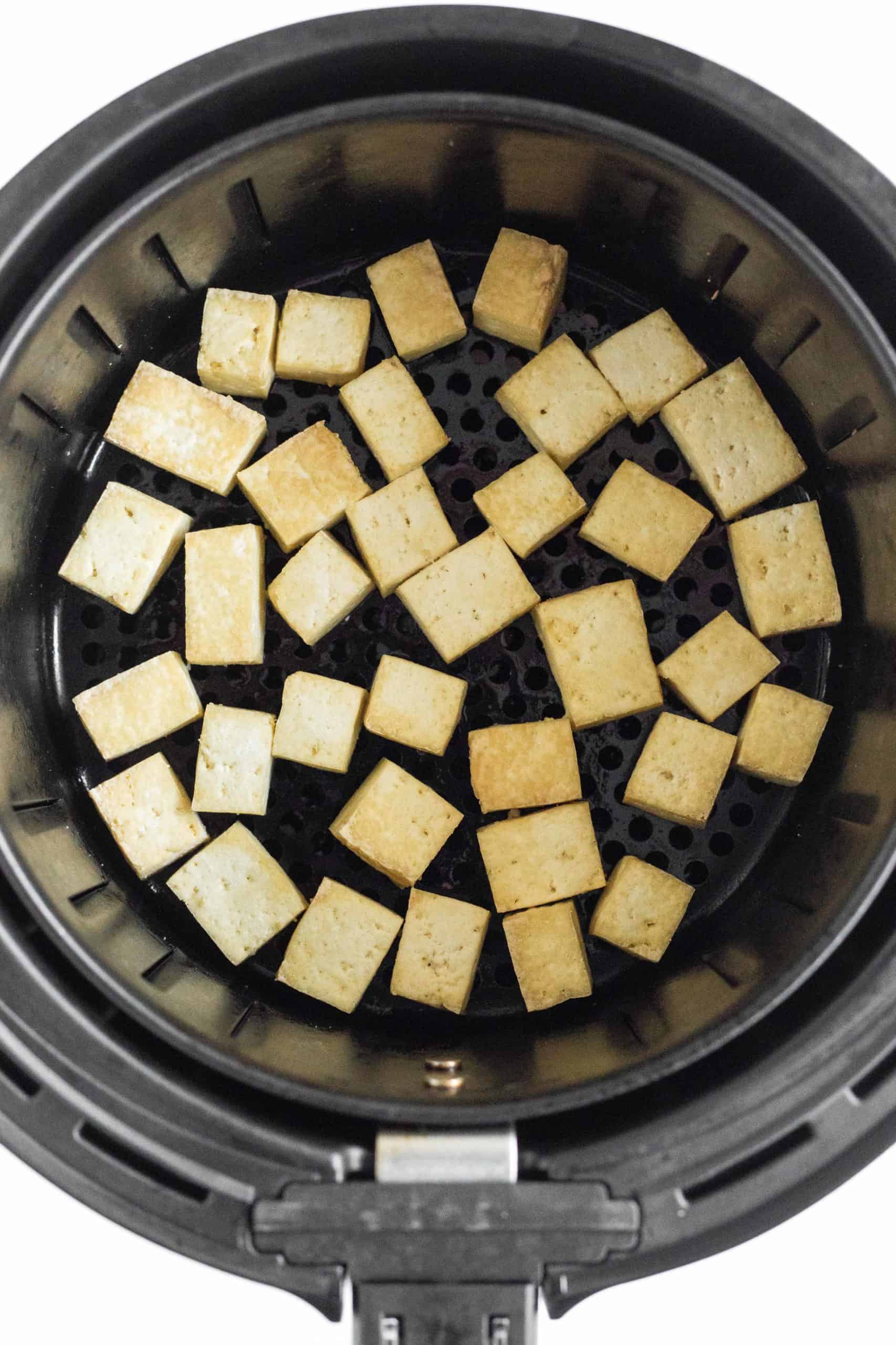 Lightly golden tofu cubes in the air fryer basket.