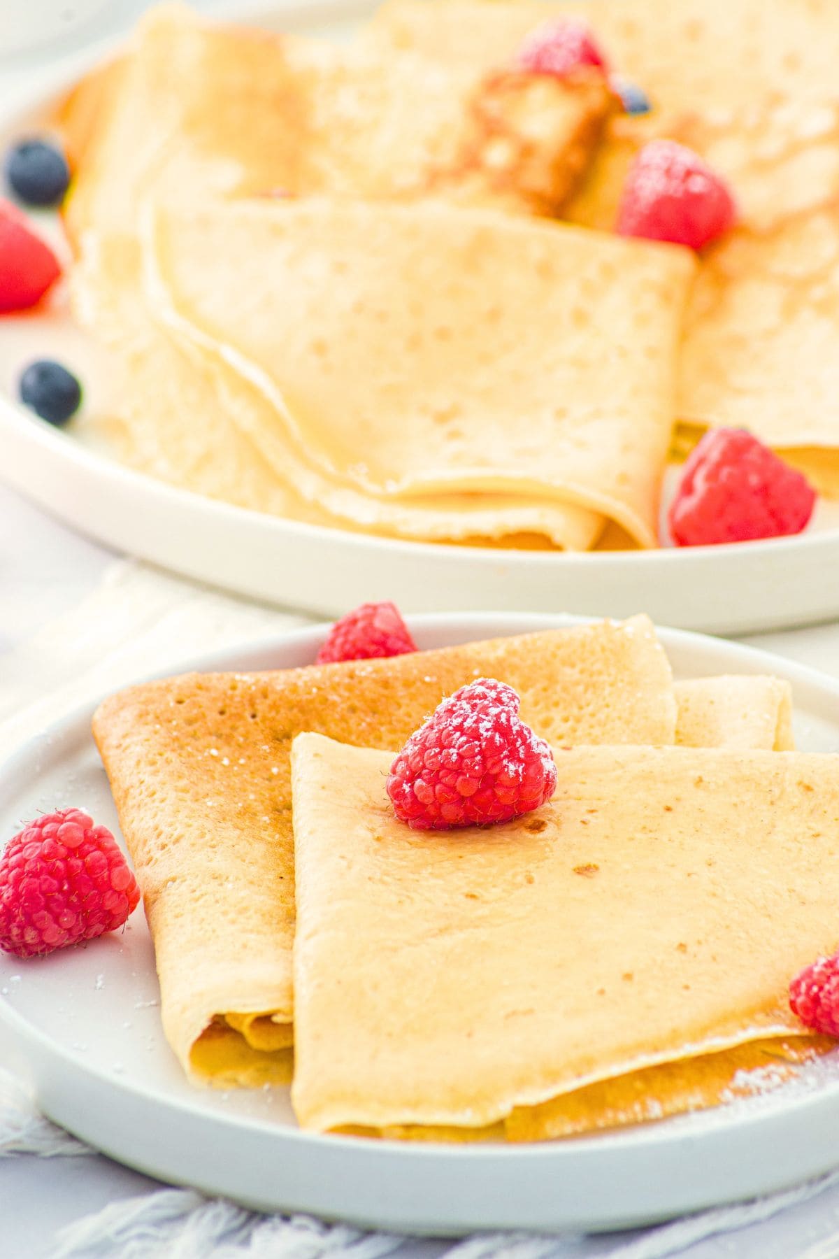 Up close view of almond flour crepes topped with raspberries and powdered sugar