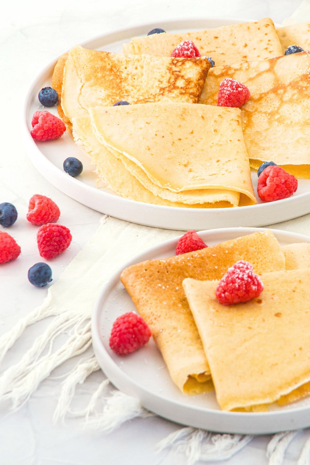 Two plates of gluten-free crepes with almond flour topped with berries.