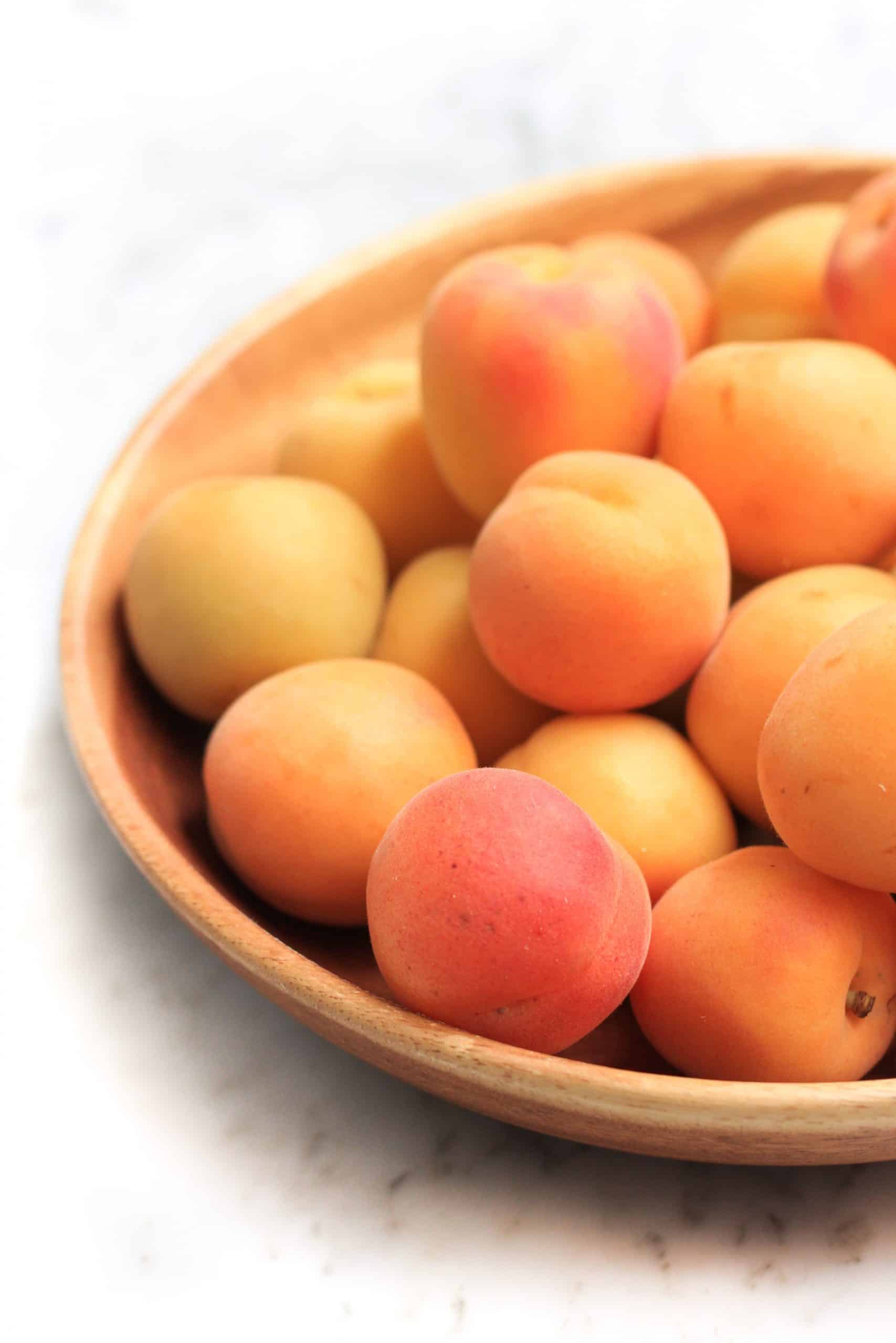 A large wooden bowl full of fresh apricots.