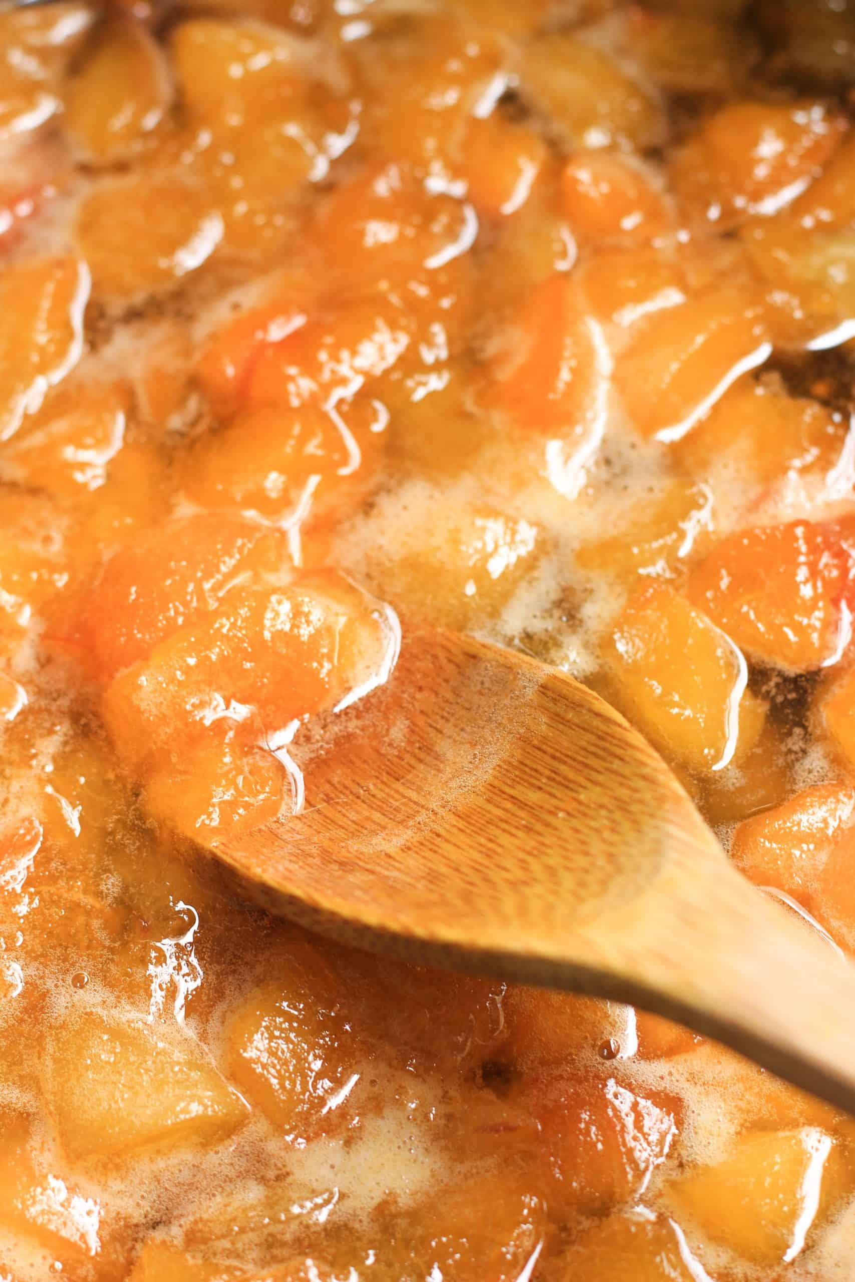 A wooden spoon mixing cooked apricots in pot