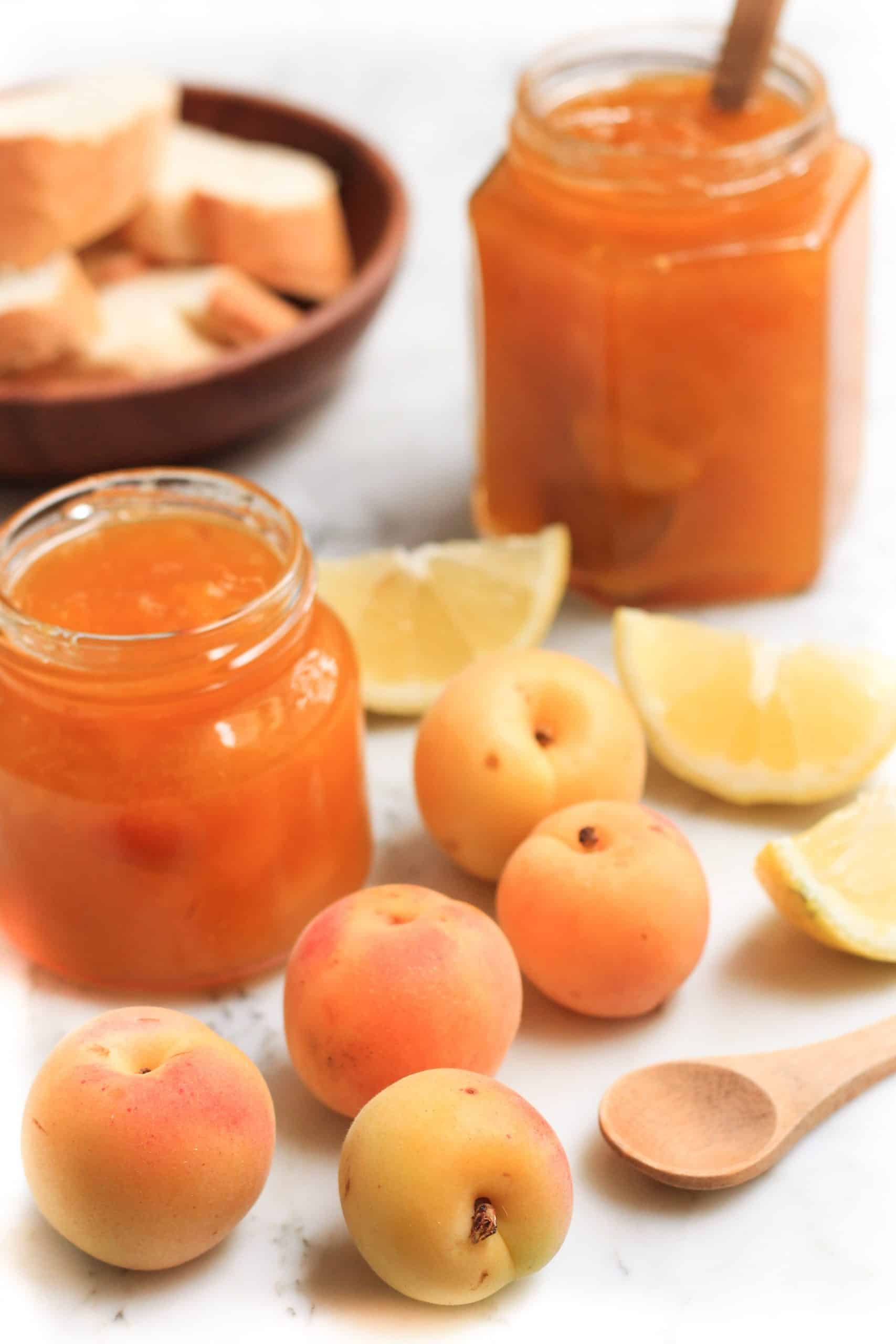 A jar of jam, fresh apricots and lemons on a marble board.
