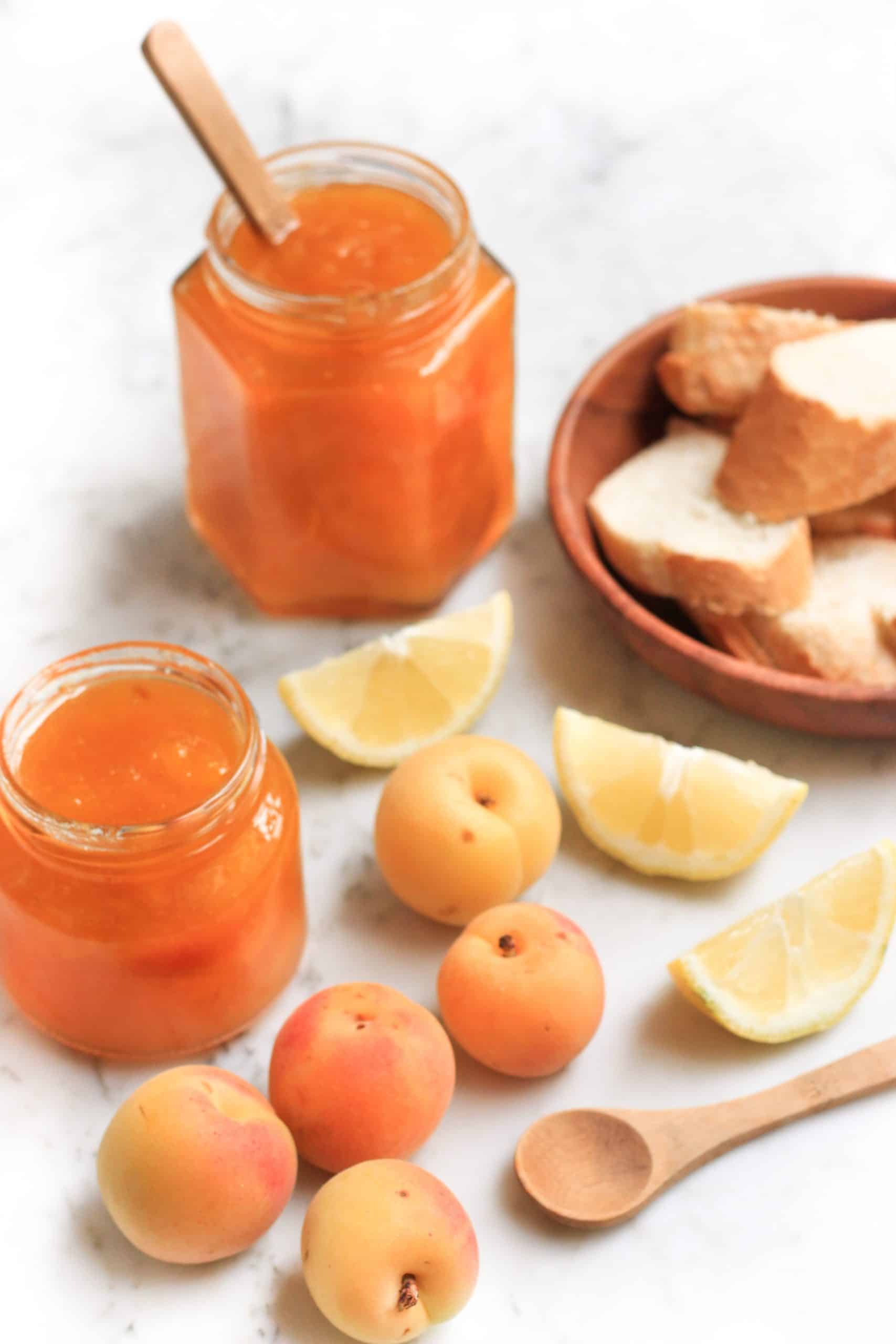 Jars of apricot jam and surrounded by fresh apricots and sliced lemon wedges