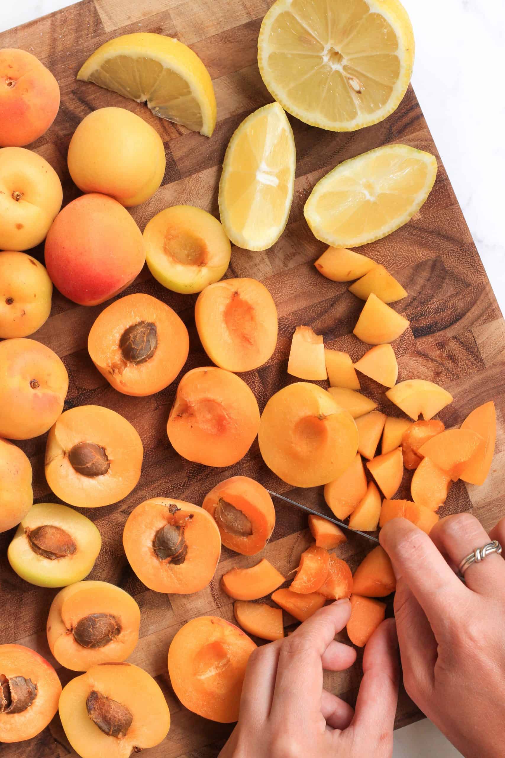 Slicing apricots into small pieces on a wooden board.