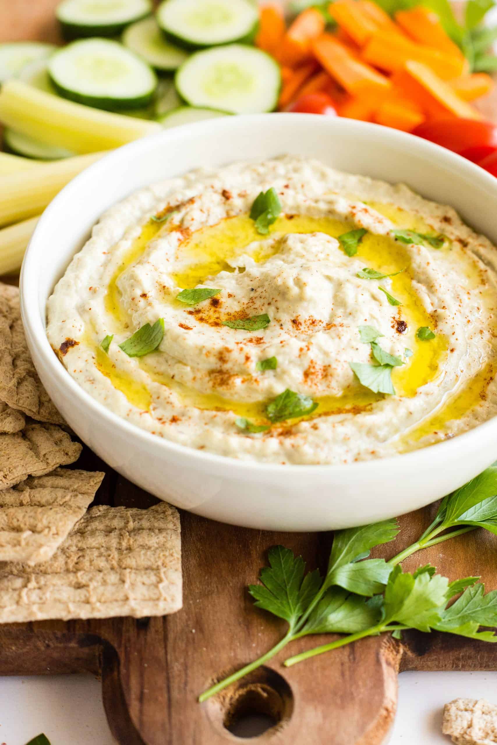 A white bowl with baba ganoush on a wooden board.