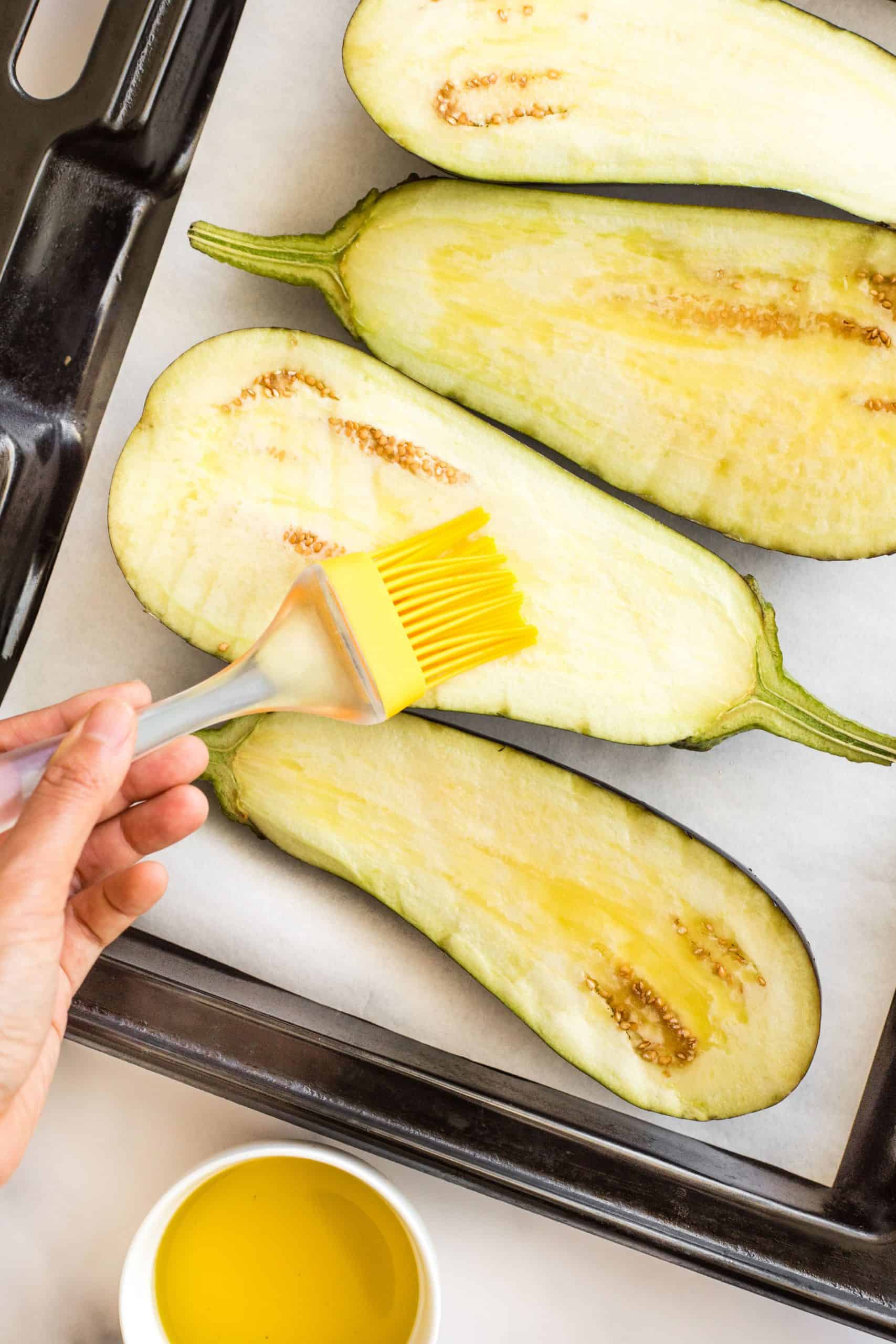 Brushing cut eggplant halves with olive oil.