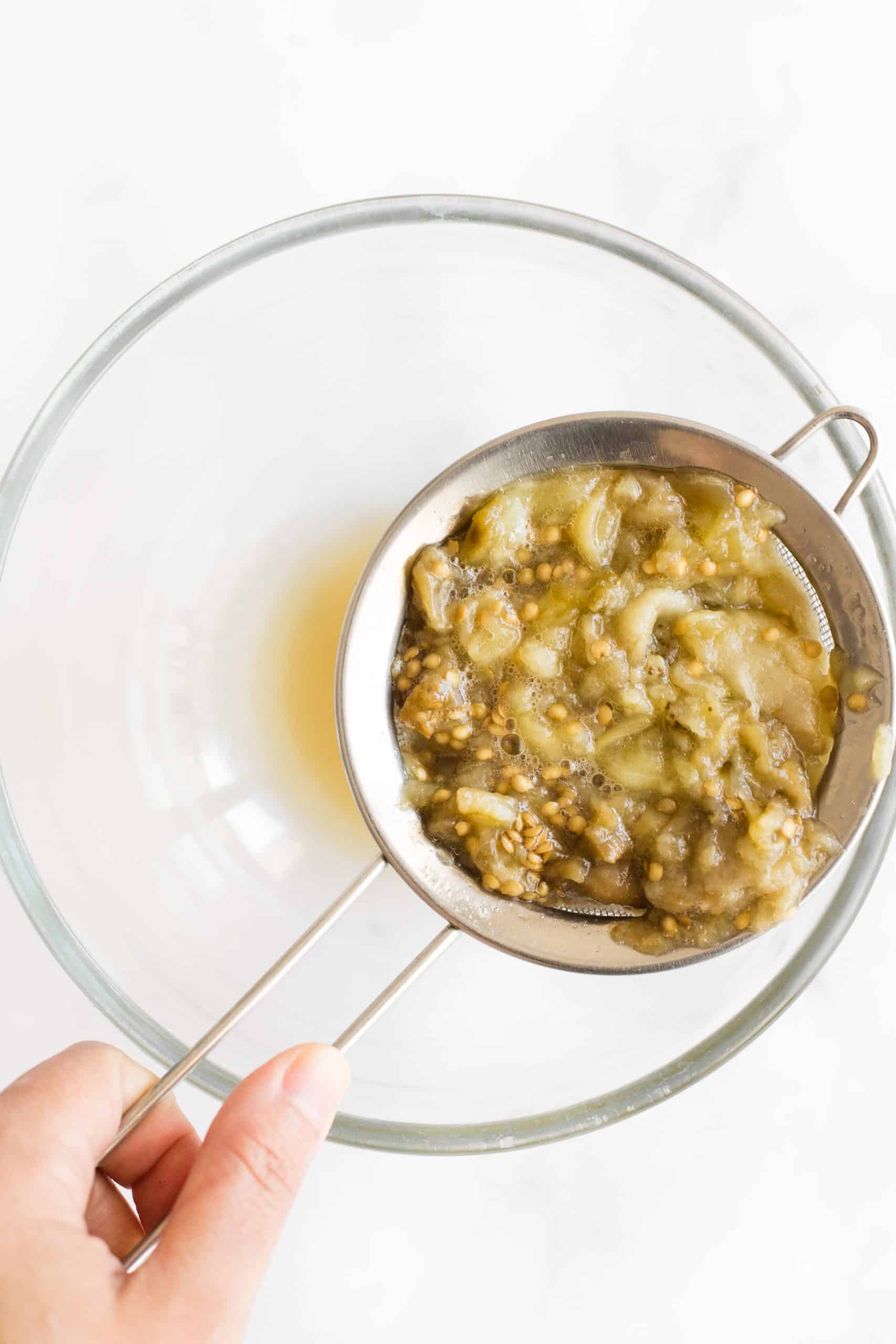 Straining the liquid from the eggplant flesh in a bowl.