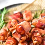 Bacon-wrapped cocktail sausages on parchment-lined plate.