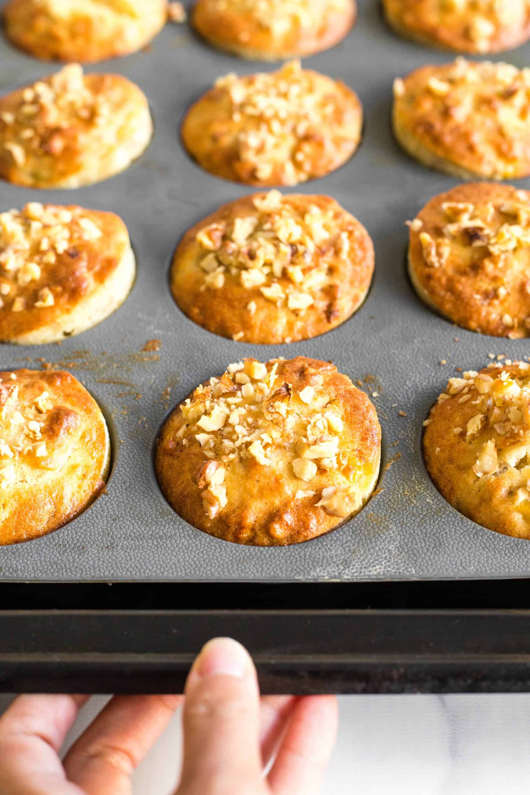 Hand holding a baking sheet with gluten-free banana muffins.