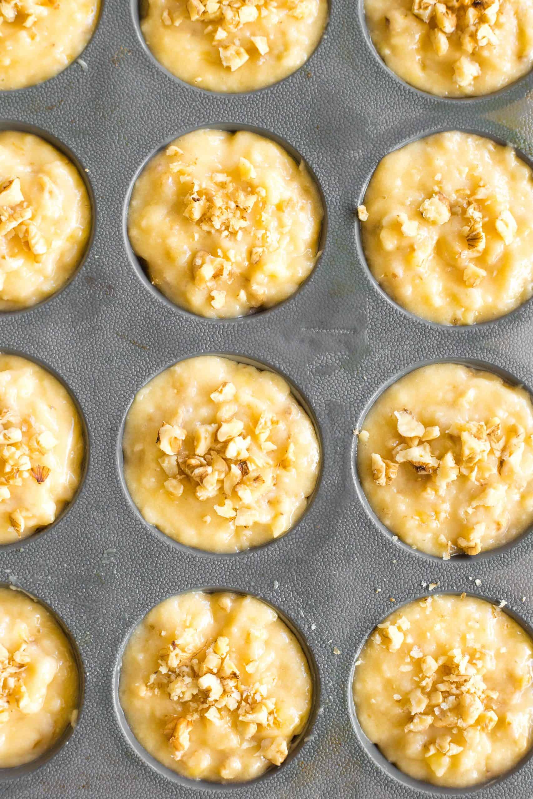 Top down shot of batter topped with walnuts in muffin mold.