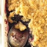 A spoon in a casserole dish with blackberry cobbler.