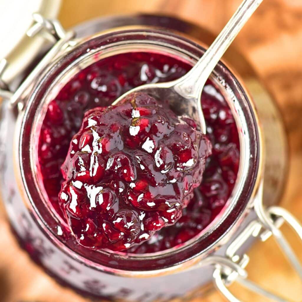 Holding up a spoonful of blackberry jam from a jar.