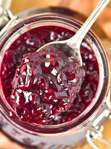 Holding up a spoonful of blackberry jam from a jar.