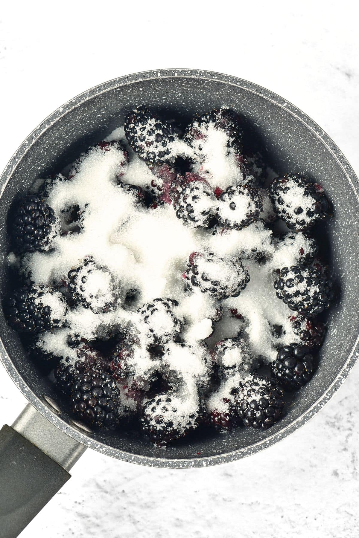 Sugar sprinkled over fresh blackberries in a saucepan.