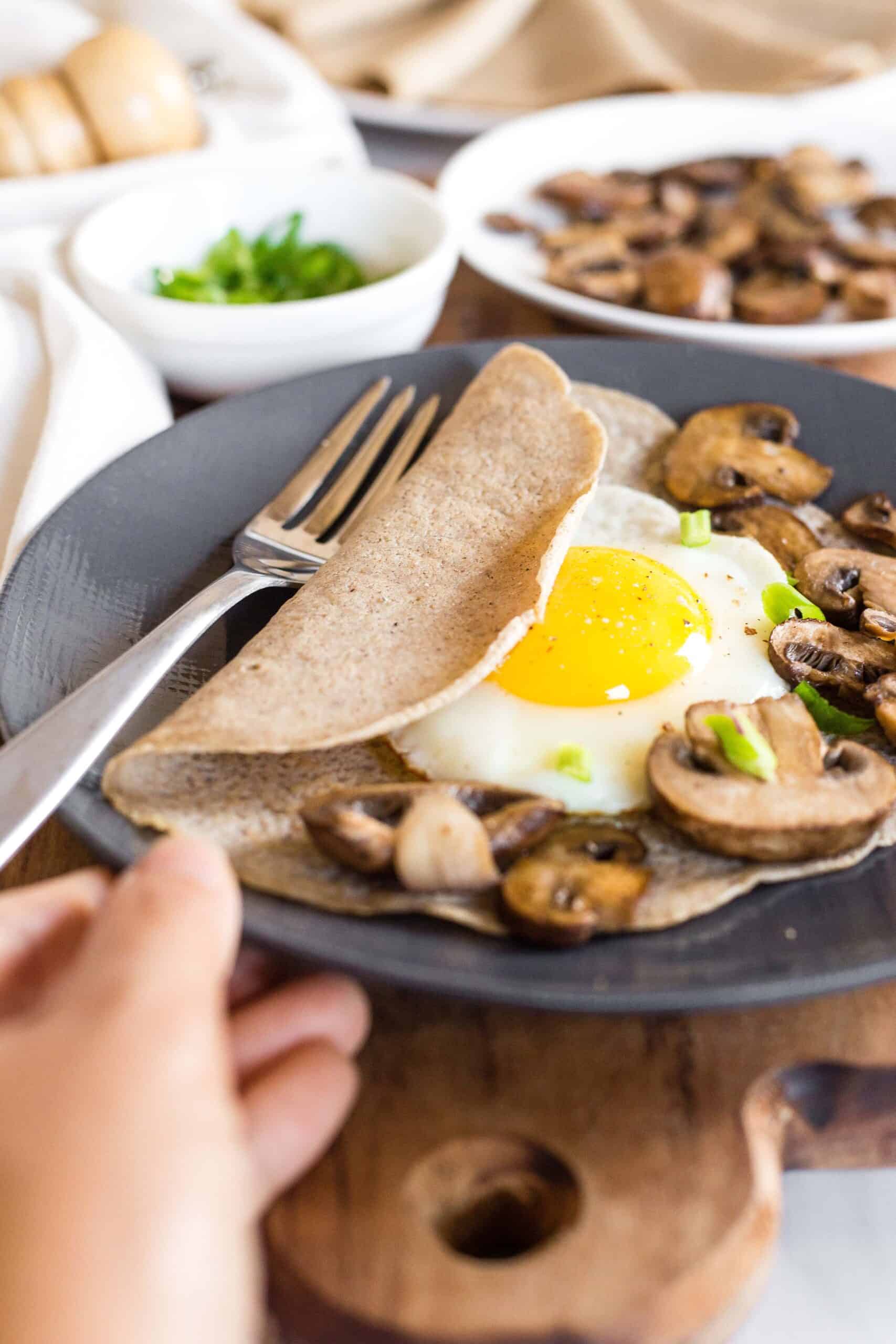 Savory buckwheat crepes with a fried egg and sautéed mushrooms on a grey plate.