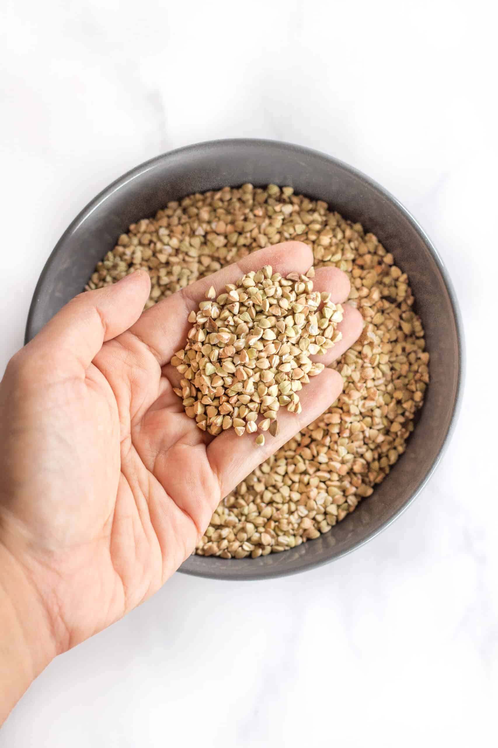 Holding up a handful of buckwheat groats from a grey bowl.