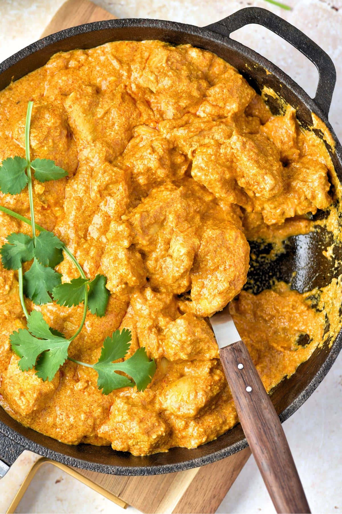 Scooping butter chicken from cast iron skillet