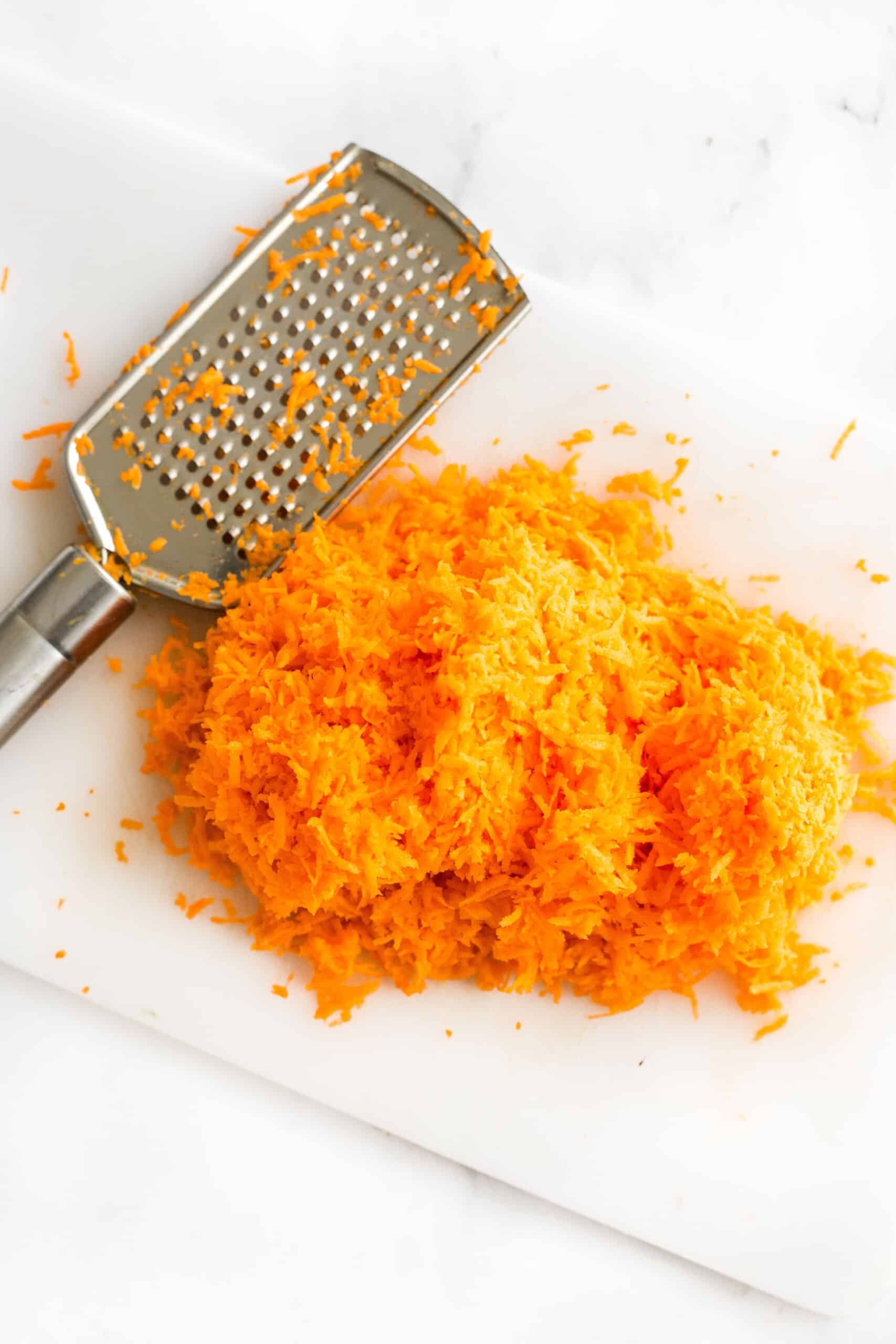 Finely shredded carrots and a grater on a chopping board.
