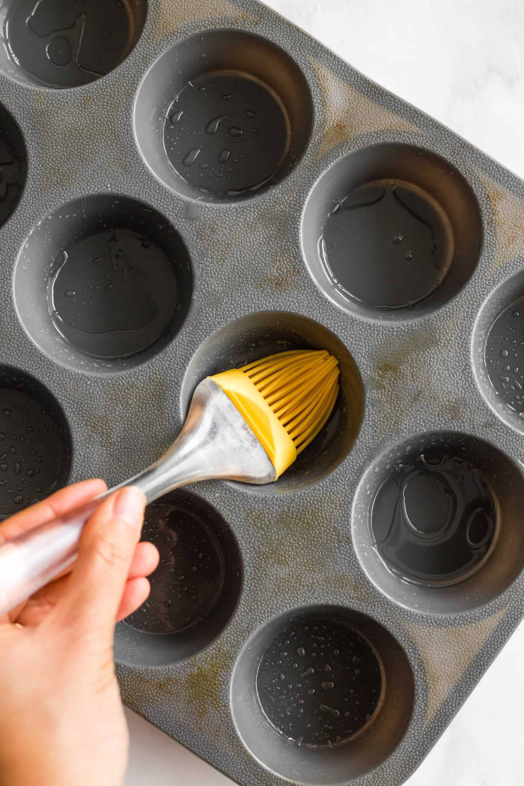Using a brush to grease a gray silicon muffin mold.