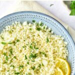 Top down view of a bowl of cauliflower rice with lemon wedges