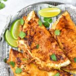 Top down view of birria chicken tacos on parchment-lined plate.