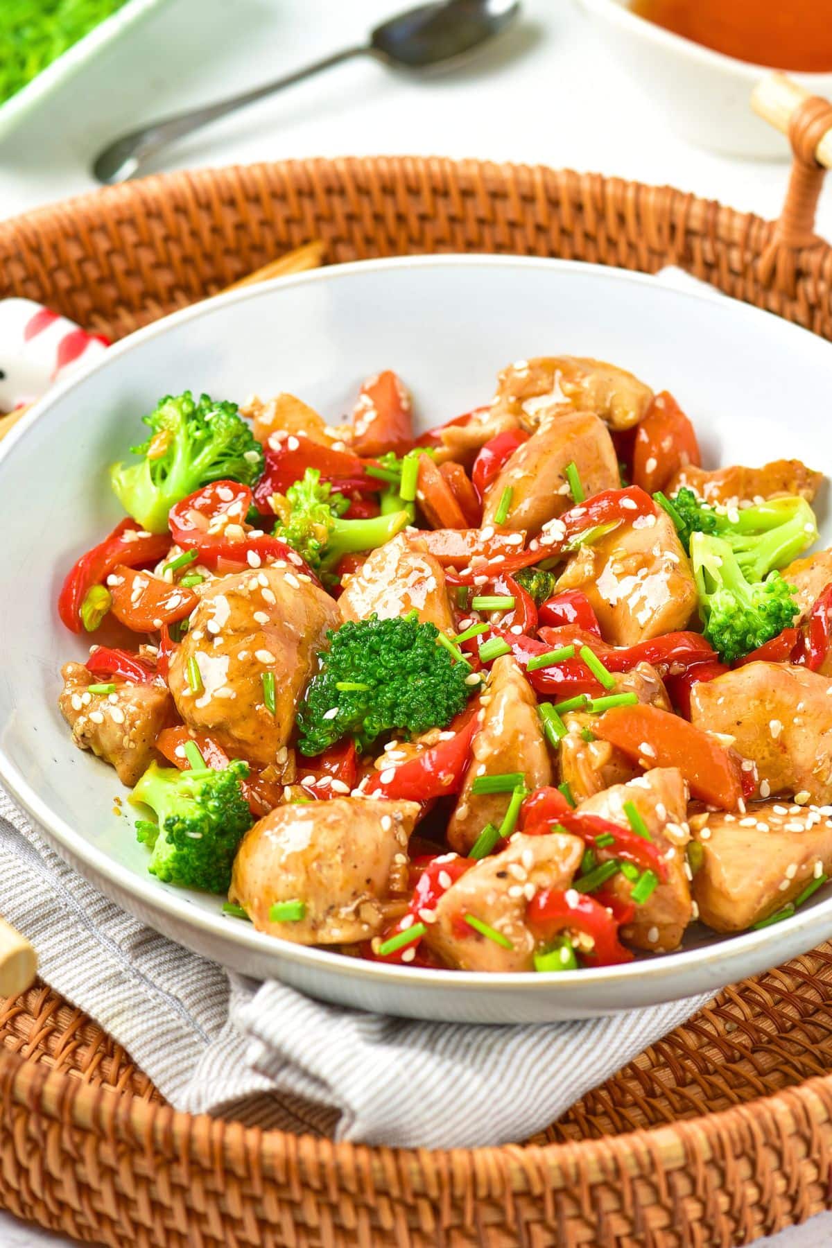 A bowl with stir fry chicken on a wicker tray.