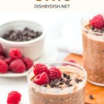 Glasses of chocolate overnight oats topped with chocolate chips and raspberries.