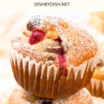 A stack of orange cranberry muffins dusted with icing sugar