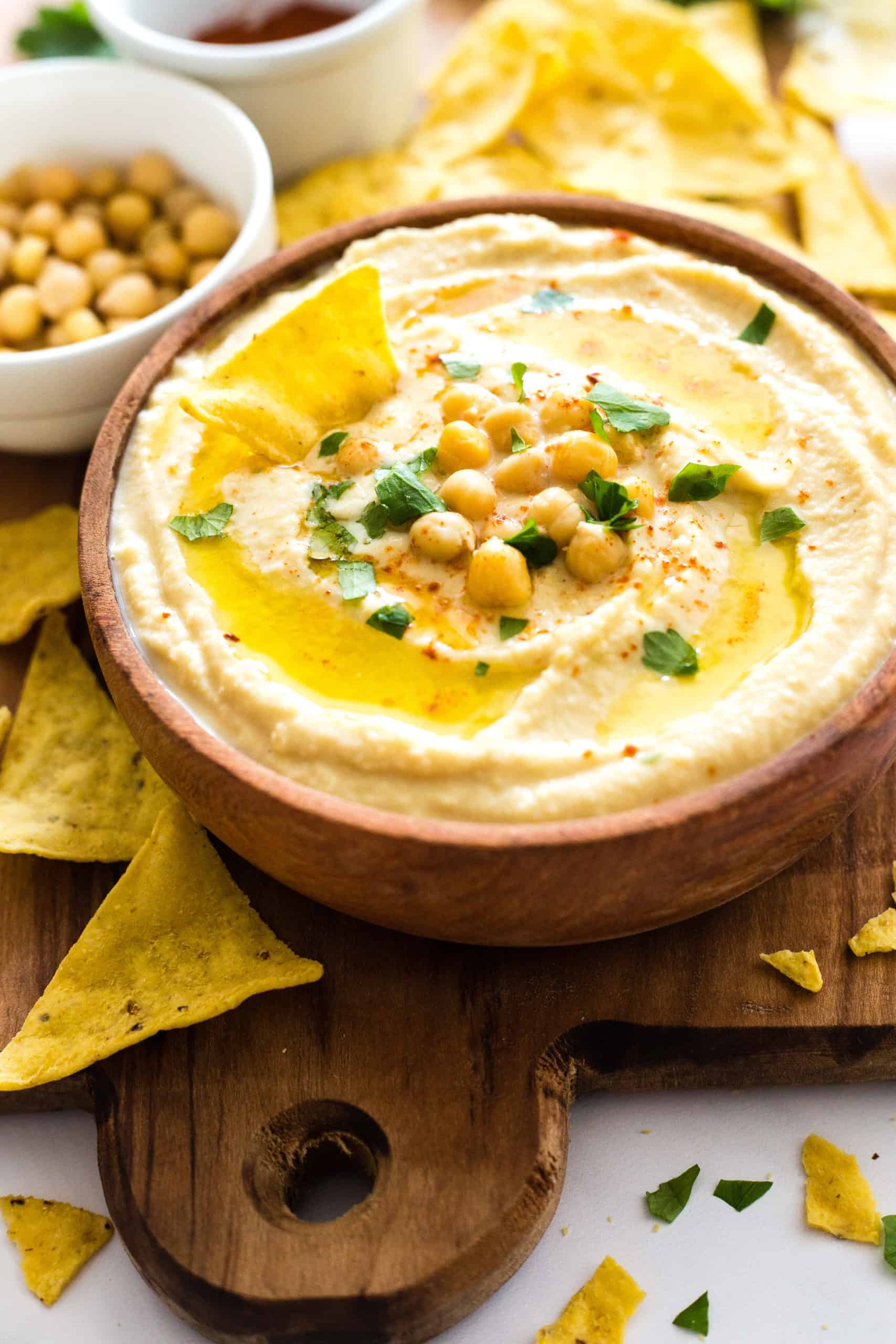 A bowl of creamy gluten free hummus and tortilla chips on a wooden board.