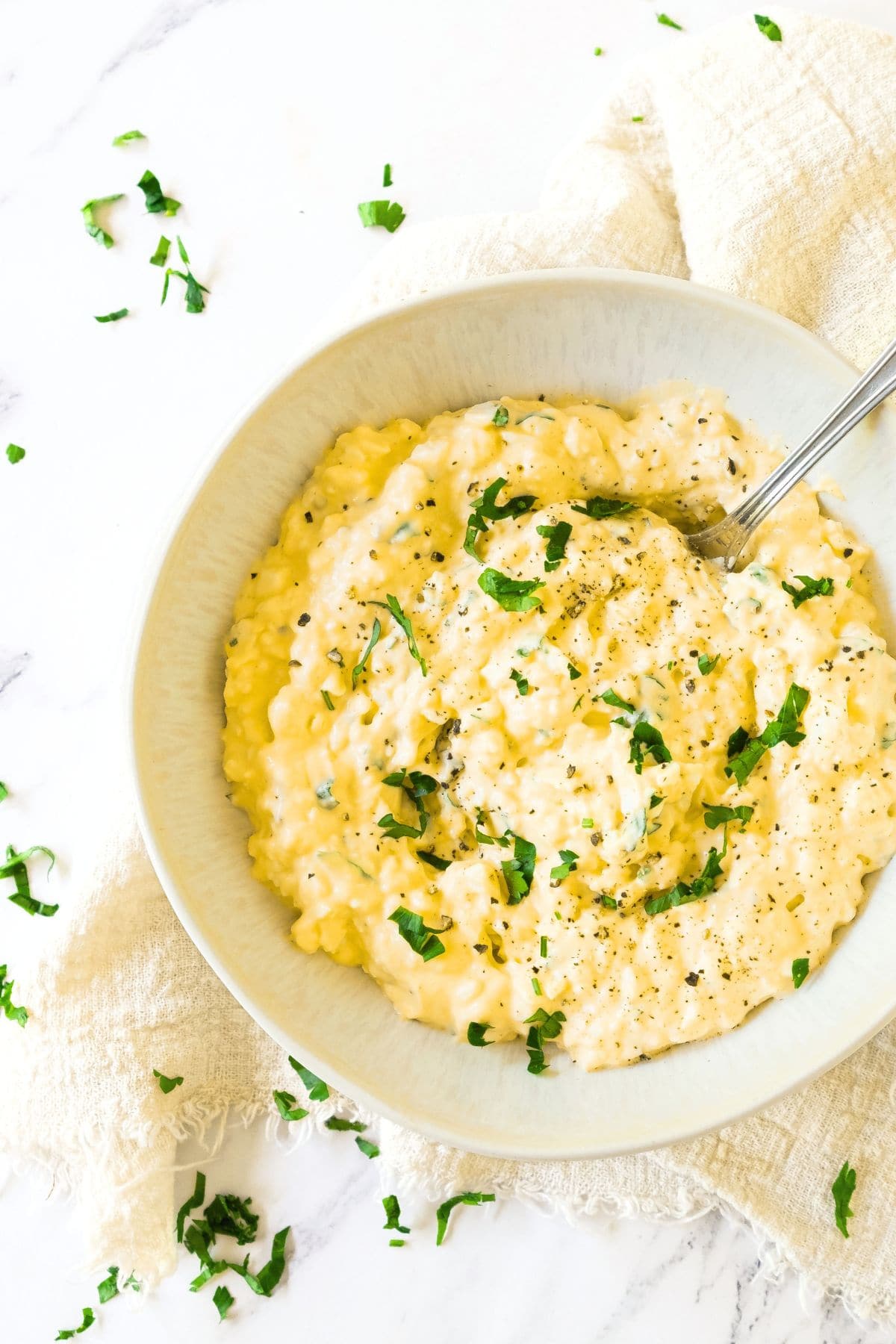 A spoon in a bowl of creamy egg salad topped with chopped parsley.
