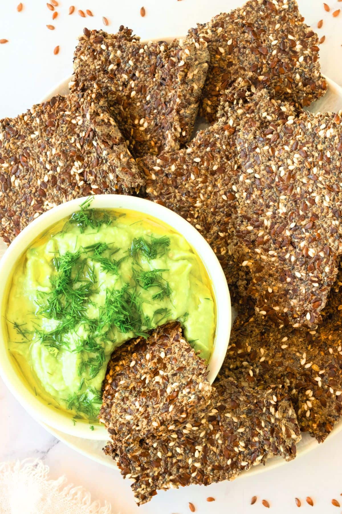 A plate of flaxseed crackers and guacamole dip.
