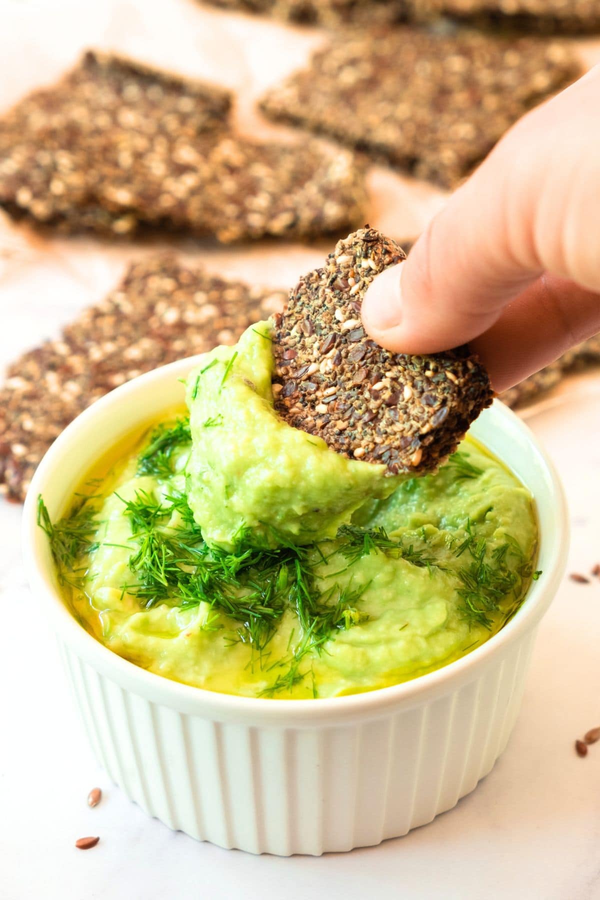 Dipping flaxseed cracker into a bowl of guacamole dip.