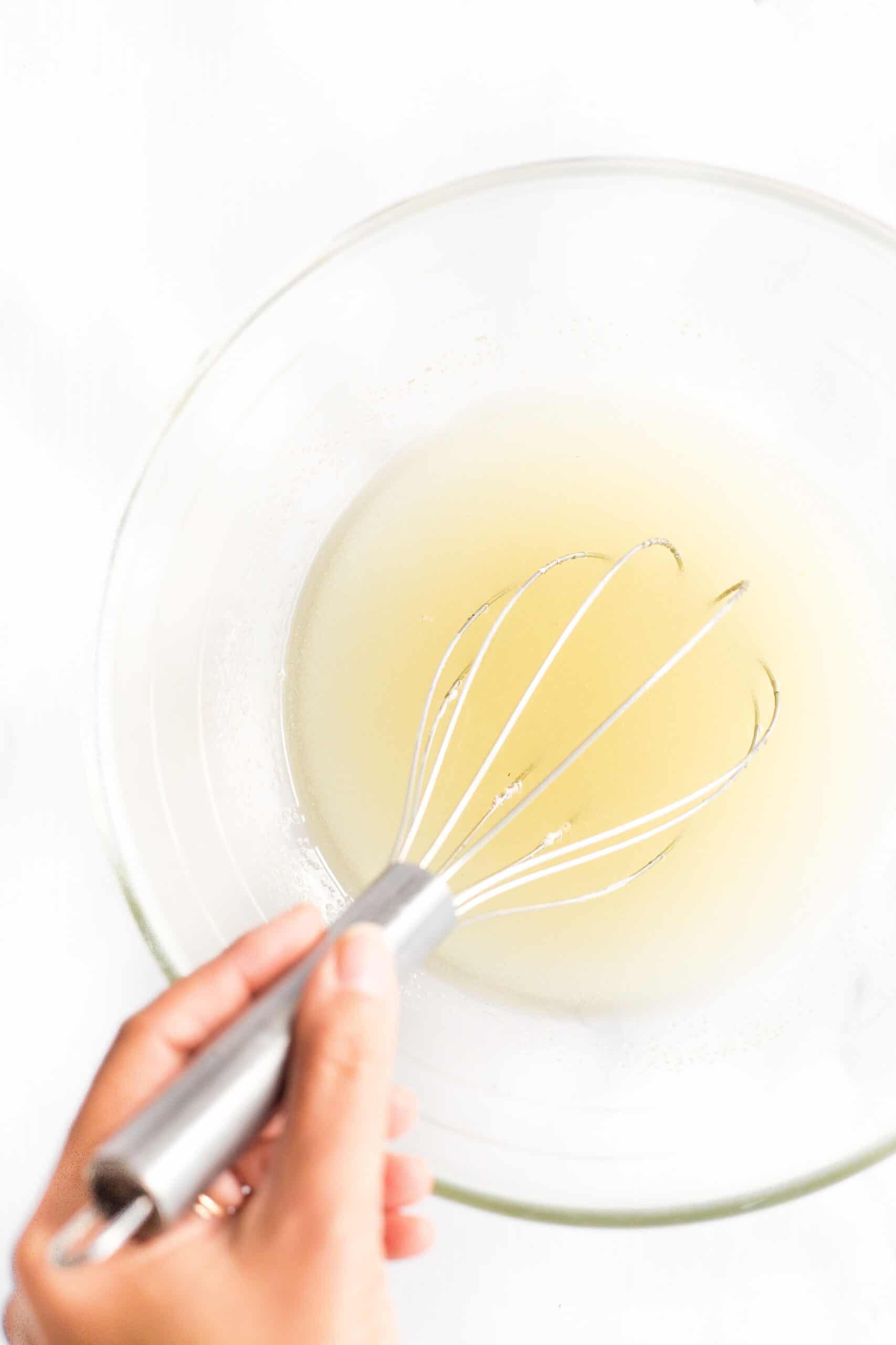 Whisking sugar and oil in a large glass bowl.