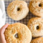 Hand holding up a bagel from wire rack.