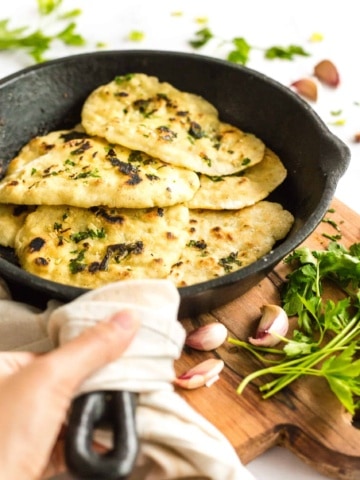 Gluten-free naan in a cast iron skillet on a wooden board