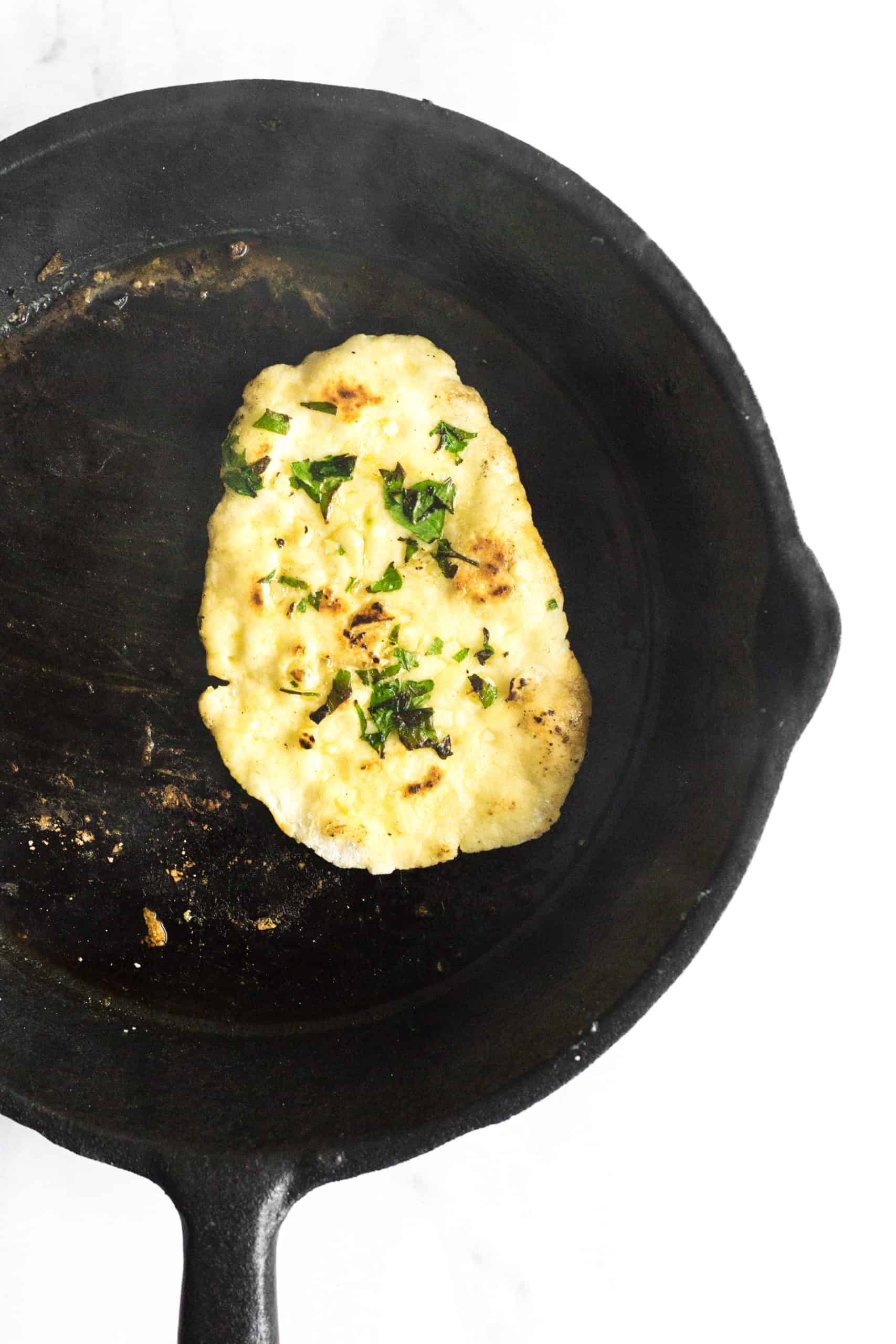 Gluten-free naan bread cooking in a cast iron skillet.